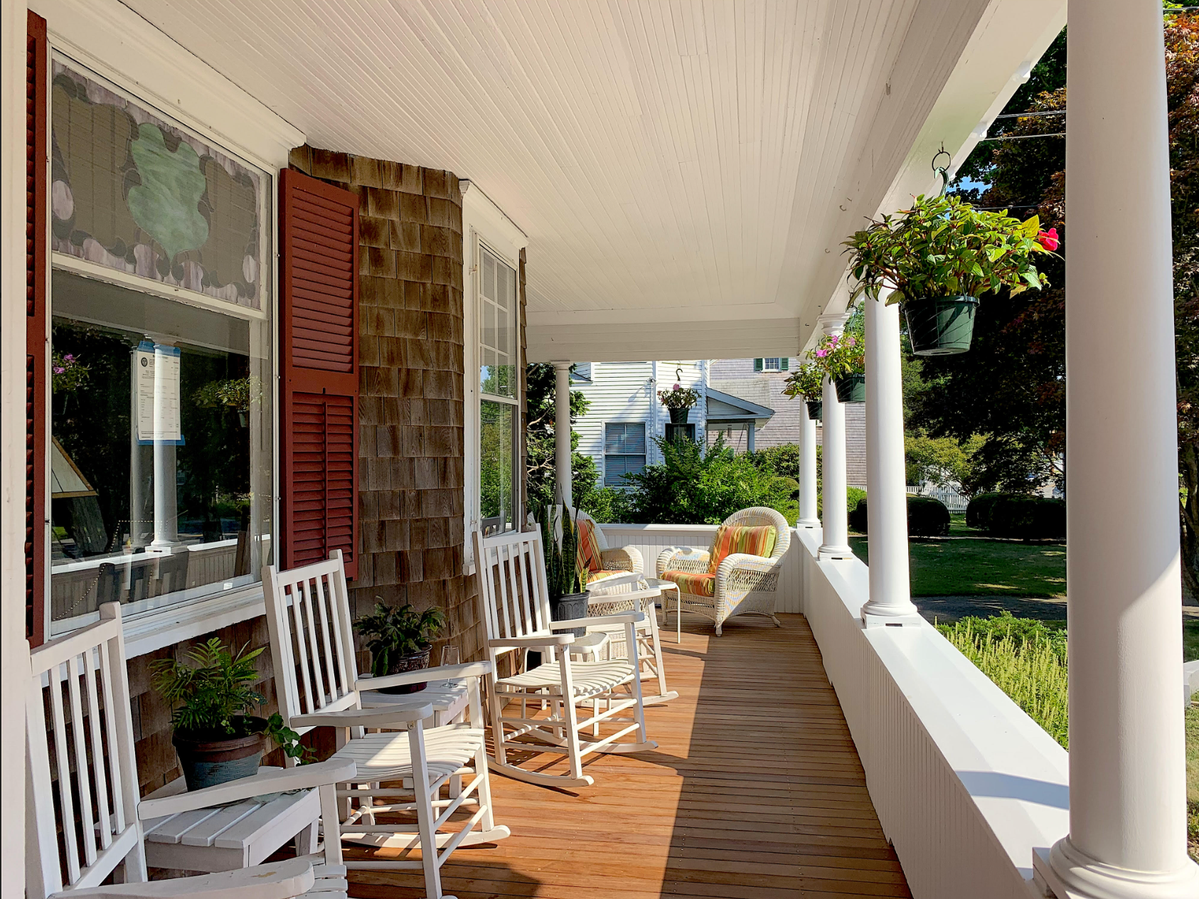 White wooden rocking chairs on a long shaded porch with green trees in the background