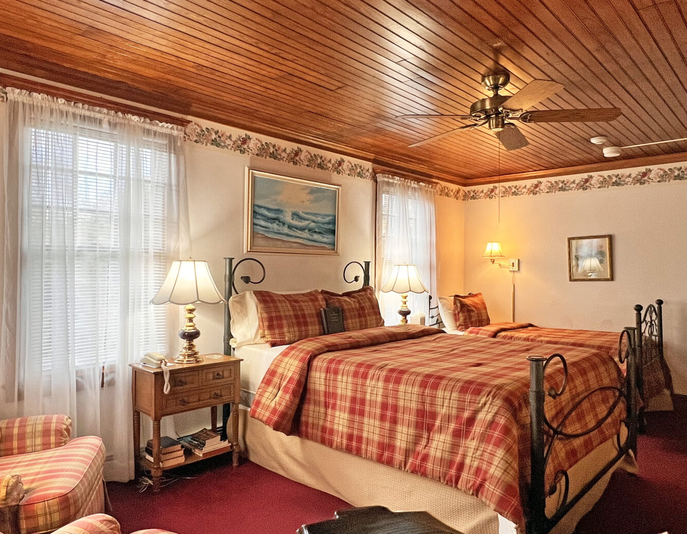 A wooden bed with burgundy and cream checkered bedding, wooden ceiling and burgundy carpet