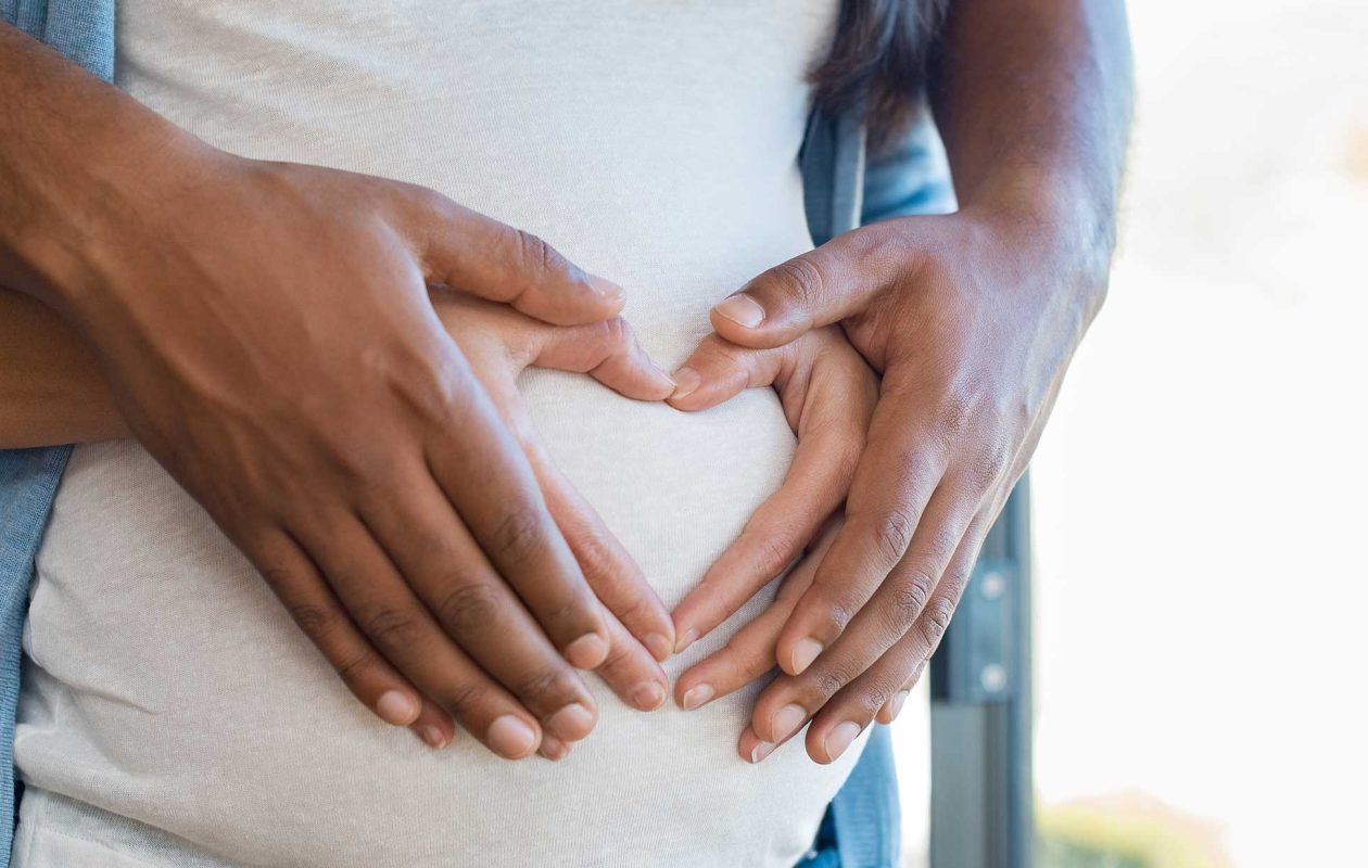 Man and woman forming heart shape with hands on pregnant woman's belly