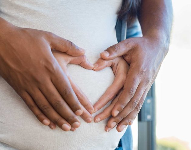 Man and woman forming heart shape with hands on pregnant woman's belly