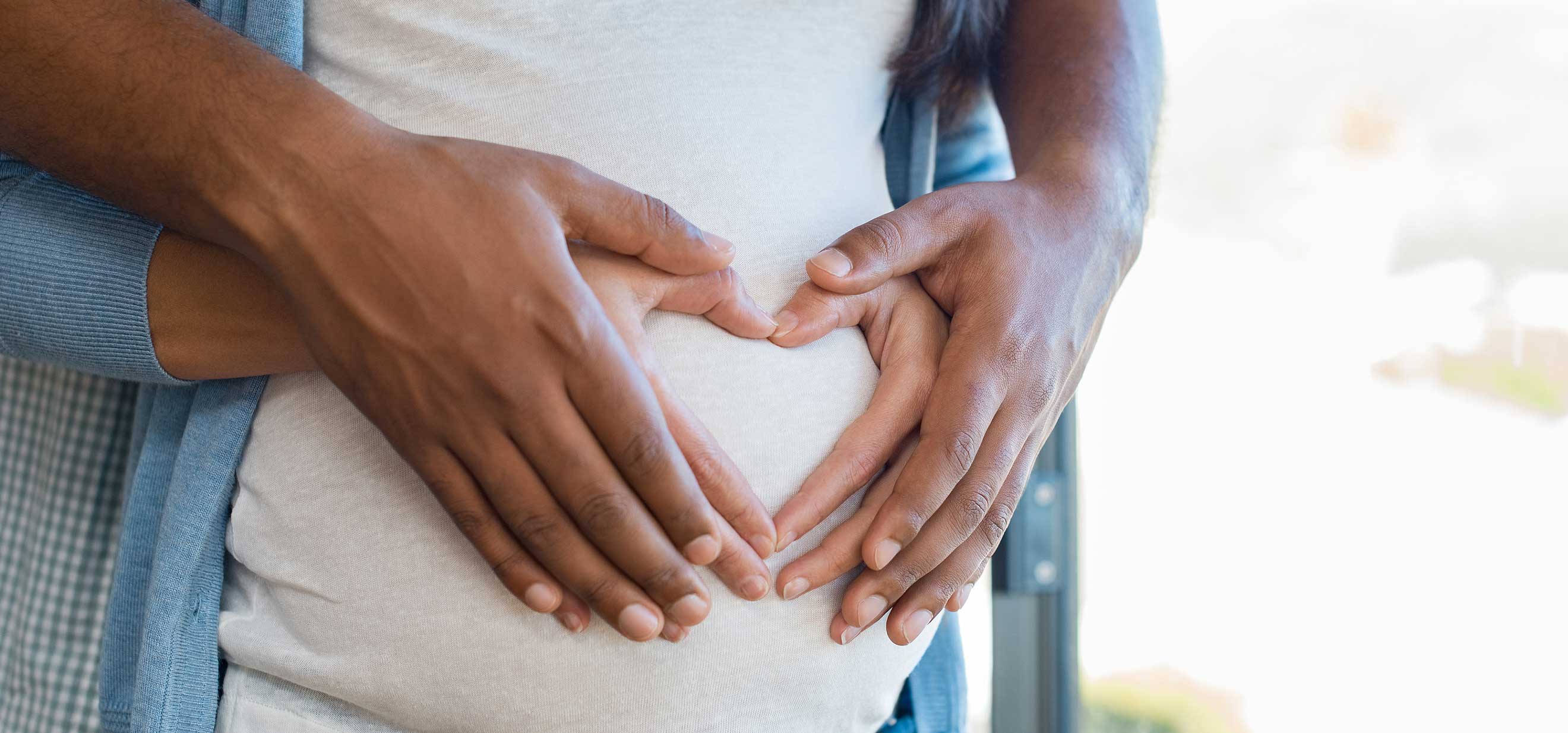 Man and woman forming heart shape with hands on pregnant woman's belly