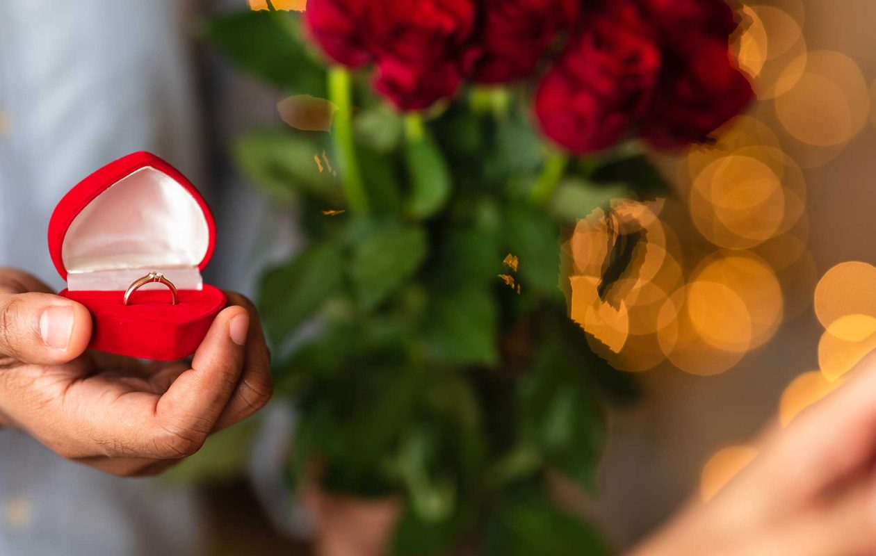 Man proposing with an engagement ring and a dozen red roses