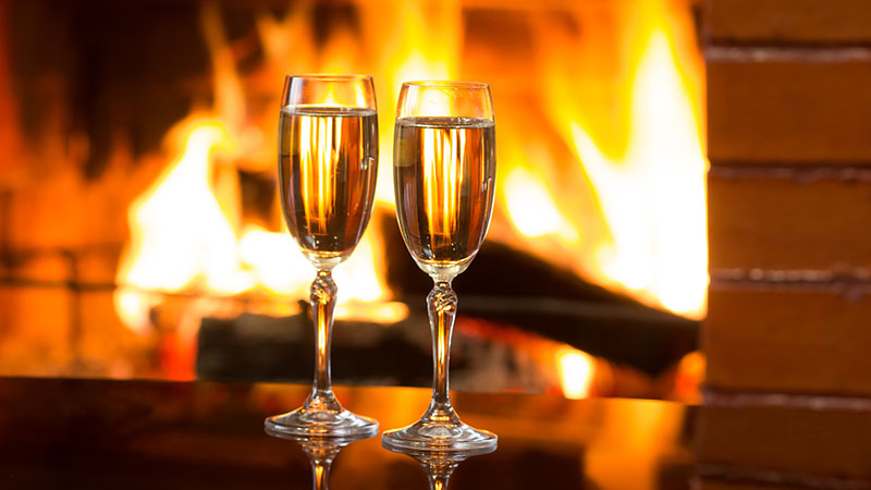 Two glasses of sparkling white wine in front of warm fireplace