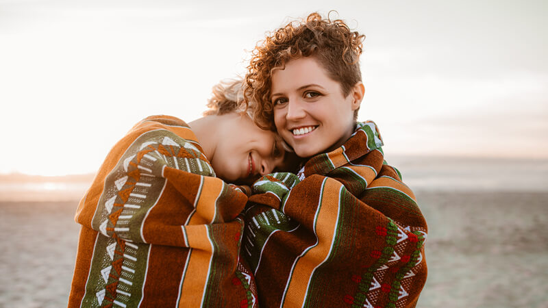 same sex couple bundled up in a blanket at sunset