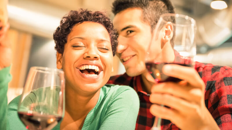 Mixed race couple laughing and holding glasses of wine