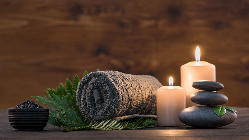 Towel on fern with candles and black hot stone on wooden background