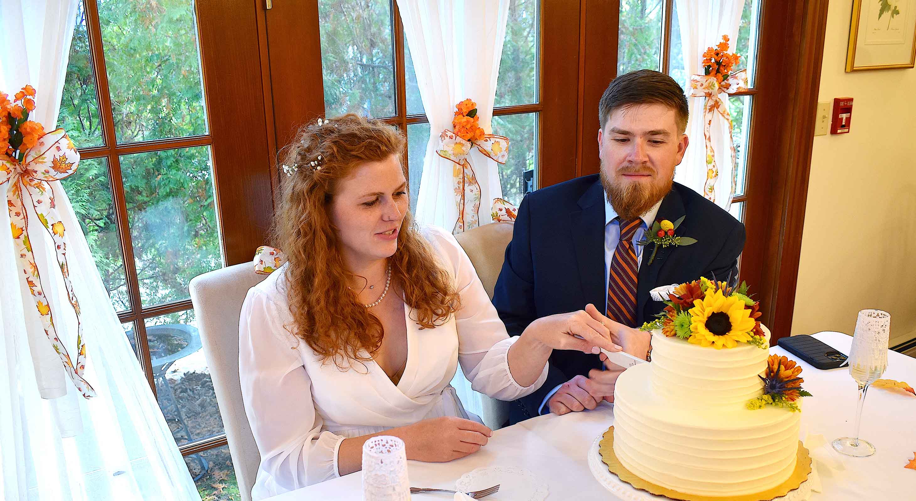 Bride and groom cutting wedding cake decorated with fall flowers during their Cape Cod elopement