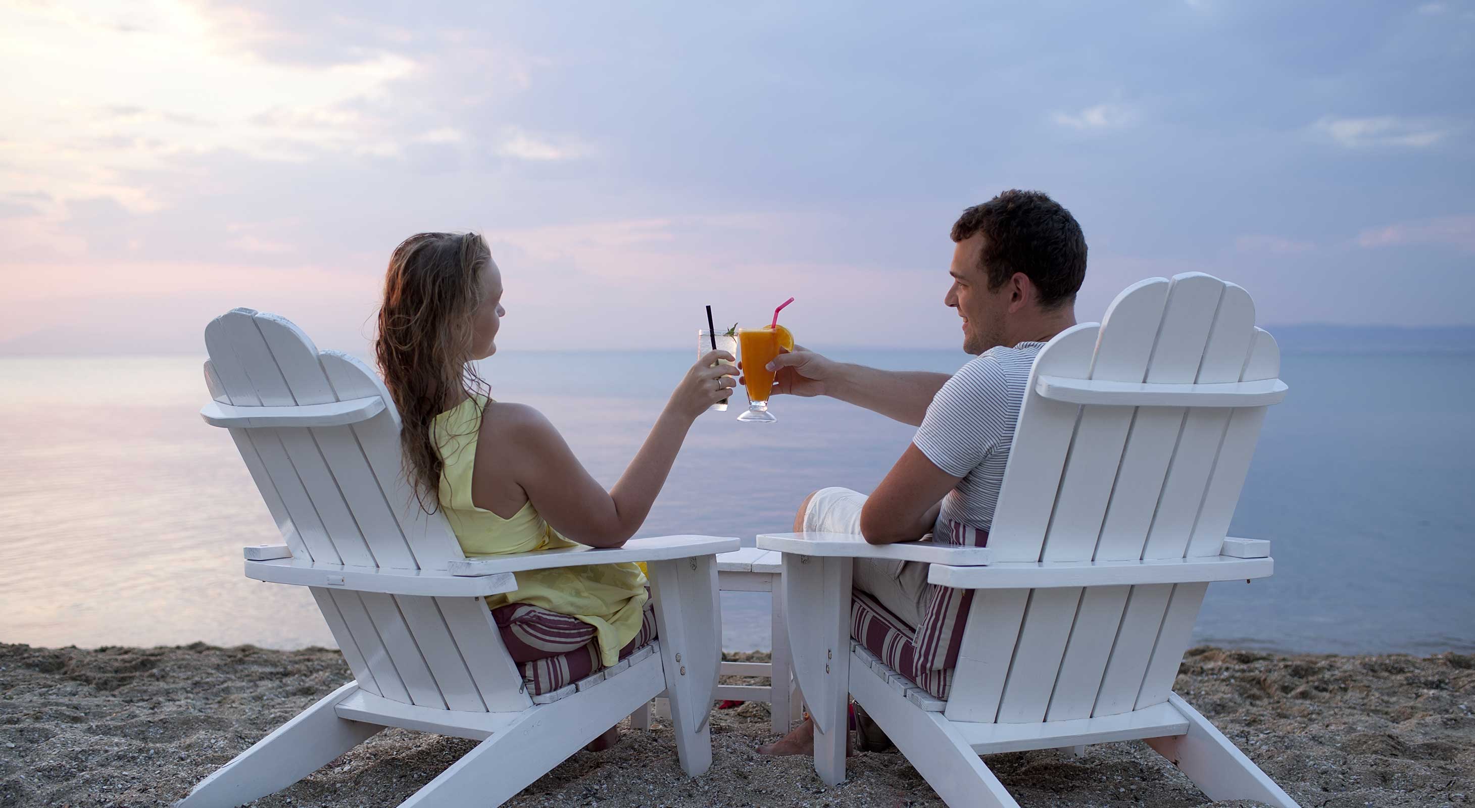 Couple in Adirondack chairs with cocktails at the beach while traveling on Cape Cod