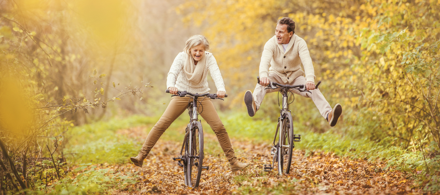 happy older couple riding bikes together having fun while fall leaves cover the ground 