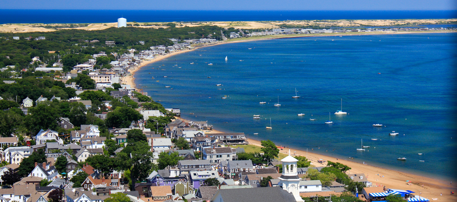 aerial shot of cape cod sandy beach curving along blue ocean and boats anchored offshore