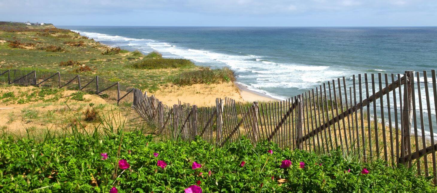 Cape Cod coastline with sandy dunes, ocean waves, and wooden fence overlooking the beach