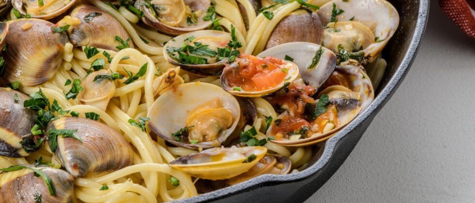 Spaghetti with clams, tomatoes, garlic, and fresh herbs fills a black skillet.